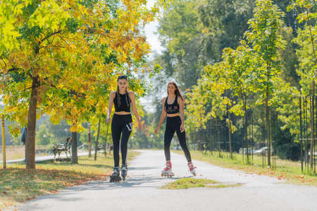 Full body portrait of happy sportswomen rollerskating in the park on a sunny day