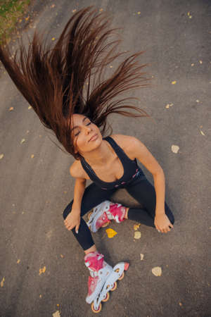 Fit sportswoman sitting on the road with roller-skates and playing with her long straight hairの写真素材