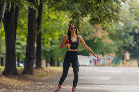 Hot athletic woman in sportswear rollerblading at the park in sunny weather.