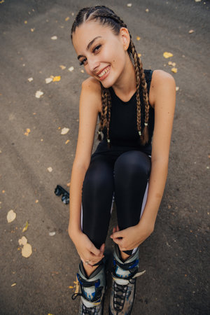 Astonishing young woman with hair braids posing in  roller skates while sitting on a road in the parkの写真素材