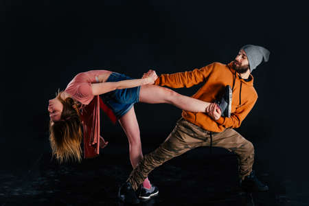 Couple dancing modern dance and showing off their leg stretch moves.Black background while the couple is dressed in urban colorful clothes.の写真素材