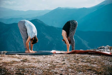 Young couple practicing yoga together on mountain peak over blue skyの写真素材