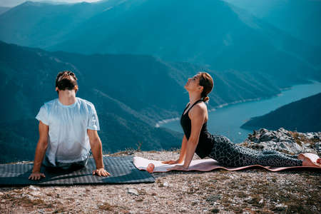 Sportive couple exercise on the rock and practicing yoga against riverの写真素材