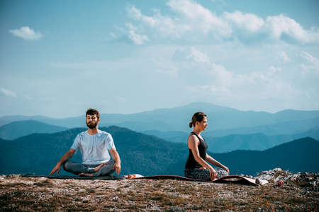 Young woman and man practicing yoga between mountainsの写真素材