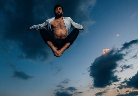 Young ballet dancer in leaping on air against blue sky with cloudsの写真素材