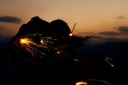 Young people playing with sparklers at night. Best friends hanging out at night on the mountain cliffの写真素材