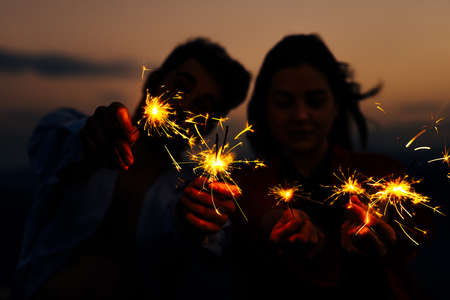 Outdoor portrait of young beautiful happy smiling couple posing on mountain. Young couple with Bengal fire in the darkの写真素材