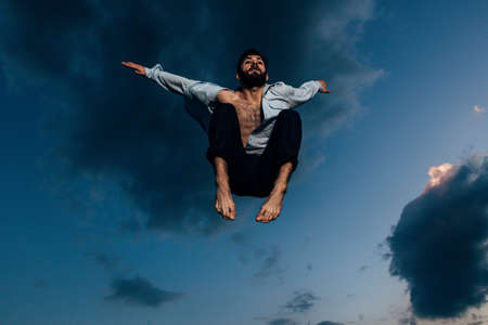 Sport, fitness, motion and people concept - happy smiling young man jumping in air over blue sky