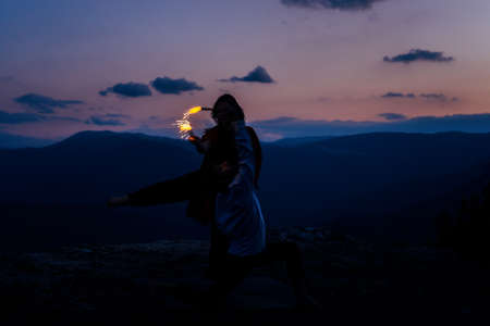 Stylish handsome ballet couple, in fashionable clothes and sparklers dancing at mountain while jumpingの写真素材