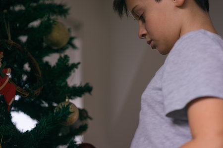 Happy boy is decorating the Christmas tree with red and yellow decoration.の写真素材