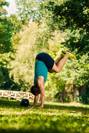Sporty young man working out while doing handstanding exercise in parkの写真素材