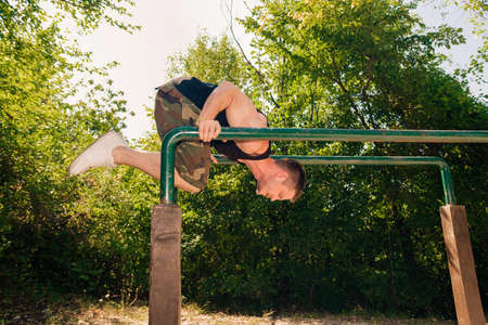 Sportive guy doing street workout on metal bars in the forest gym