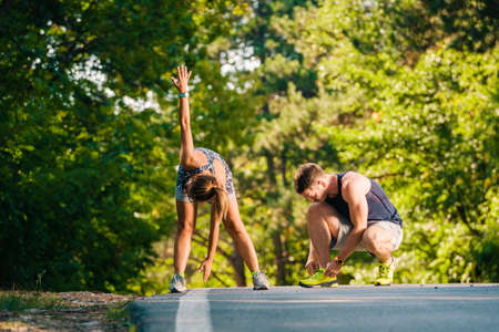 Fitnes and healthy couple exercising on the road near the forestの写真素材