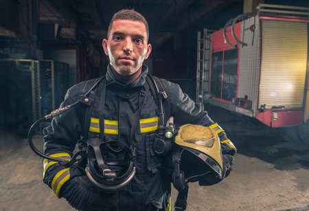 Portrait of a fireman wearing firefighter turnouts holding helmet ready for emergency service.