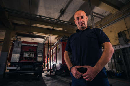 Portrait of handsome firefighter standing against trucks at fire station