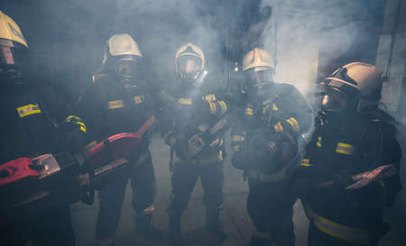 Group of firemen with gas masks standing in the middle of the chainsaw's smoke