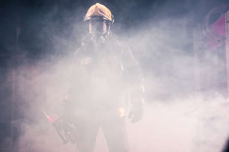 Portrait of young fireman standing and holding a chainsaw in the middle of the chainsaw's smokeの写真素材