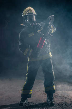 Portrait of a fireman wearing firefighter turnouts and helmet. Dark background with smoke and blue light.の写真素材