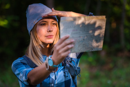 Young woman walking alone in the woods holding a map. Hiking concept in the mountain in summerの写真素材