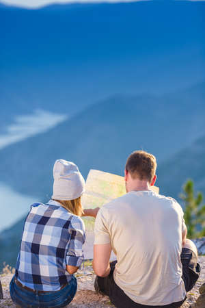 A couple checking their position on the map and enjoying the peak of the mountain, cliff at sunset.