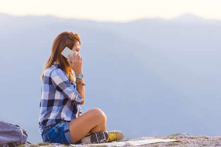 A lady talking on the phone and marveling the view from the mountain top at sunset.の写真素材