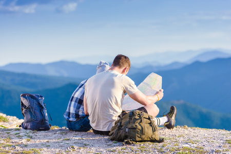 A couple checking their position on the map and enjoying the peak of the mountain, cliff at sunset.の写真素材