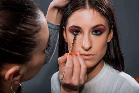 Cool young woman having her makeup done by a proffesional artistの写真素材
