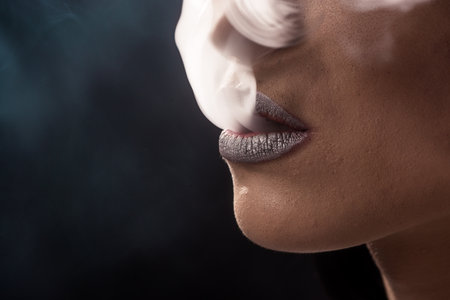 A young, pretty woman smokes a cigar on a dark backgroundの写真素材