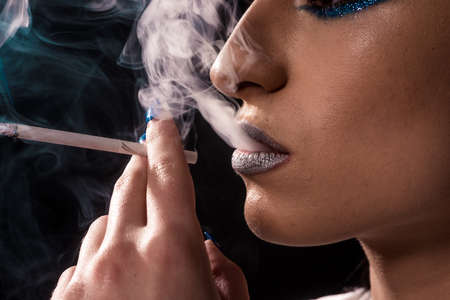 Portrait of beautiful woman with cigarette on black backgroundの写真素材