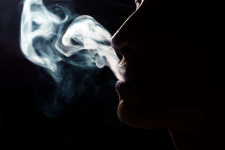 Beautiful woman is smoking a cigarette, isolated on black backgroundの写真素材