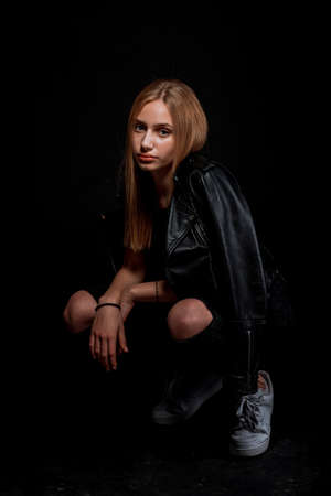 Body shot of a stylish woman posing in black leather jacket and white sneakersの写真素材