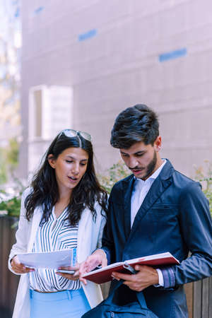 Front view of a happy couple of executives walking and talking on the street with an office building in the backgroundの写真素材