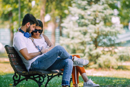 Couple of young lovers sitting close on wooden bench in park on a dateの写真素材