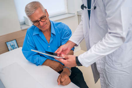 Middle aged caucasian doctor explains to his senior patient his blood pressure readings while standing next to him.の写真素材