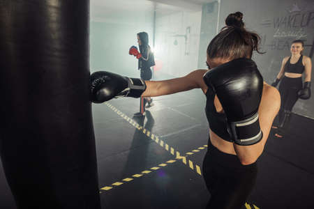 Young woman in black boxing gloves training with punching bag in gym.の写真素材