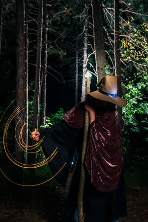 Young wizard holding a glowing staff in his hand preparing to cast a spell in the woodsの写真素材