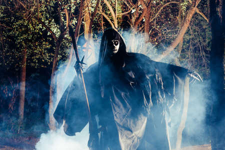 Grim Reaper standing in the fog at night with his scythe.