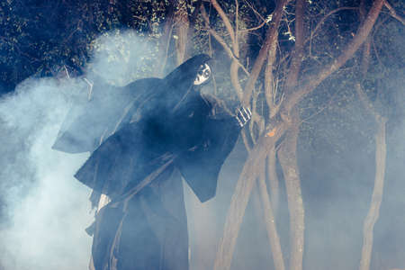 Portrait of the angel of death, grim reaper while standing in a mystical wood at night.