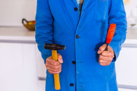 An old age handyman in overall is standing in the kitchen with his toolsの写真素材
