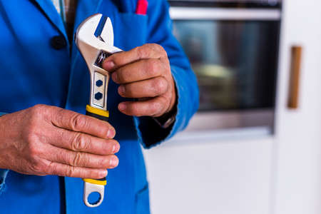 Handyman standing in the kitchen and shows his wrenchの写真素材