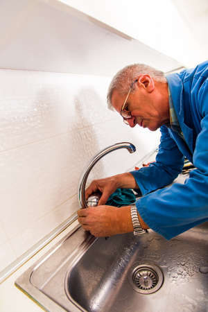 Repairman in blue working suit is holding pilers in his hands and fixing the tapの写真素材