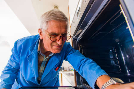 Repairman is standing in the kitchen and fixing the ovenの写真素材