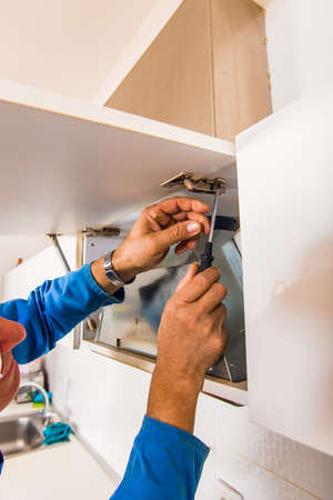 Old age repairman is fixing the kitchen cupboard with screwdriverの写真素材