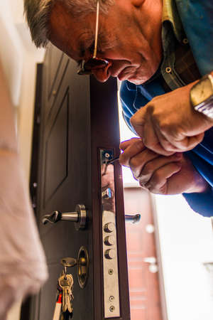 Mature craftsman is standing and fixing the door with screwdriverの写真素材