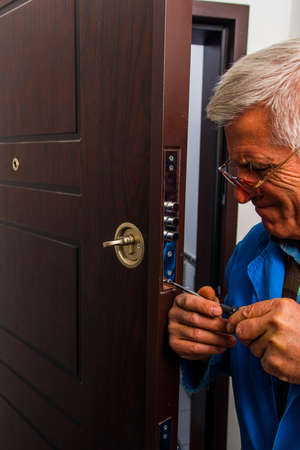 Mature laborer is fixing the door lock