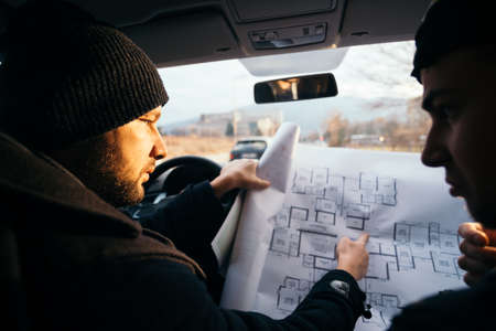 Two violent robbers sitting in a car looking at a blueprint of the building they want to rob while proudly showing off their guns.の写真素材