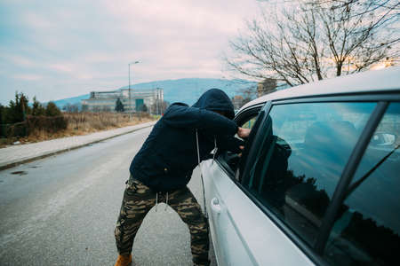 Carjacker aggressively attacking a car owner with a gun, trying to extort money.