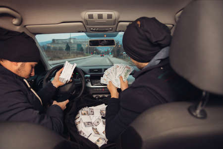 Two happy bank robbers celebrating their successful hit while sitting in the car they used for the...