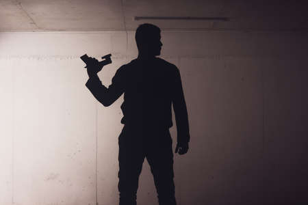 silhouette of an armed man holding his gun and pointing with his laser beam at a target.の写真素材