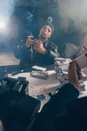 Dangerous burglars counting stolen cash on the table with a weapon near themの写真素材